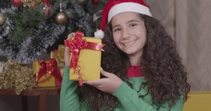 Caucasian brazilian girl, curly hair, christmas clothes. holding present and giving smiles, happiness for having won a present. Christmas, Merry Christmas. 4K 60fps Premium cinematic video