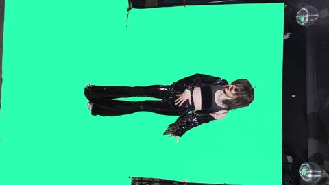 vertically. travesty actor in black flared trousers and a black leather jacket, dances and sings in full growth on a green background.