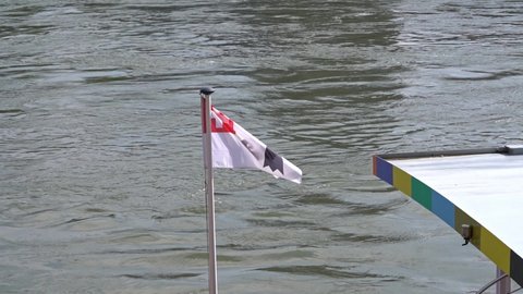 Combination of Swiss flag and flag of City and Canton Basel waving form ship moored at border of Rhine River. Slow motion movie shot April 27th, 2022, Basel, Switzerland.