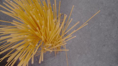 SUPER SLOW MOTION, CLOSE UP, PROBE LENS: Top down view of falling spaghetti on gray background in slow motion. Falling spaghetti close up. Detailed view of scattered raw pasta.