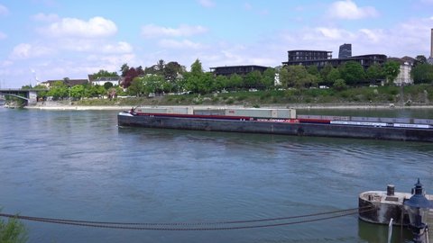 Cargo container ship named Grindelwald on Rhine River at City of Basel on a blue cloudy spring day. Movie shot April 27th, 2022, Basel, Switzerland.
