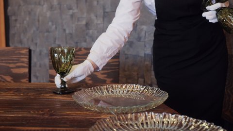 Unrecognisable Waitress serving festive table with wine glasses in restaurant. Woman waitress preparing a set dishes and glasses for event banquet