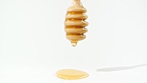 Honey Dripping to a Honey Dipper. Liquid Honey Flows on the Isolated White Background. Healthy Food Concept. Macro Shot.