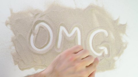OMG, Oh my God Top view draw on the sand. Caucasian hands write text in beige sand. Vacation and travel. Beach on vacation. Sand painting. Creativity from natural materials.