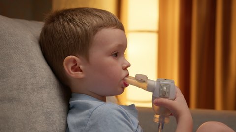Treatment of pneumonia with nebulizer at home. Child has respiratory infection or bronchitis, and he is breathing heavily. Blond Caucasian child with asthma problems inhales with tube in his mouth.