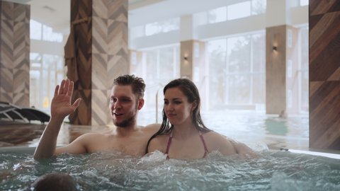 spouses are relaxing in jacuzzi in modern spa center, children are playing near, happy family weekend