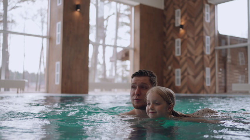 happy childhood and parenthood, father is teaching is little daughter to swim in swimming pool