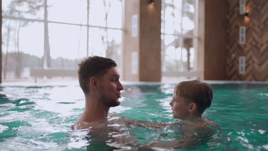 happy preschooler boy is playing with his dad in swimming pool, family is resting together in weekend or vacation