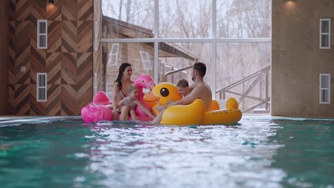happy family in water park, parents and children are floating on inflatable flamingo and duck and laughing