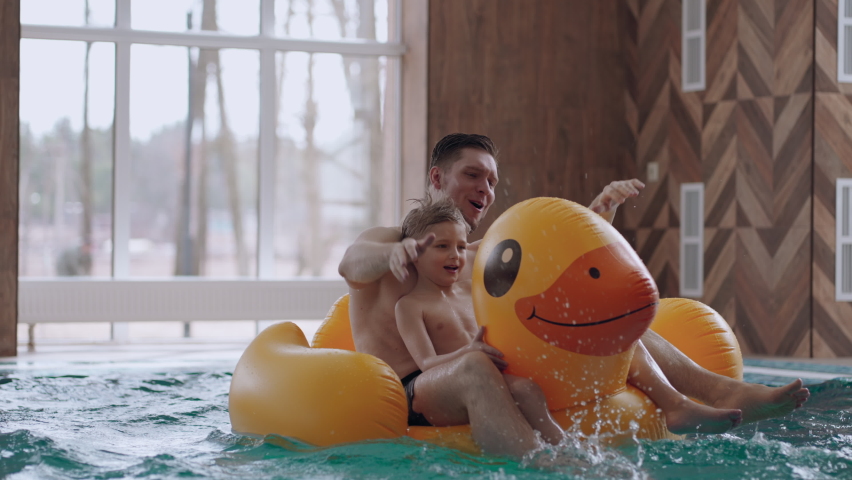 family entertainment in swimming pool, father and little son are floating on funny rubber duck and laughing