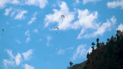 Group of tourists paragliding on parachute in front of the clouds above the mountain at Manali in Himachal Pradesh, India. Tourists lifting off from the mountain for paragliding experience. 