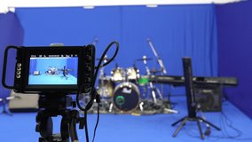 Selective focus and close-up of the video camera screen that capturing instruments with a drum kit, keyboard, and stereo, arranged on the blue screen backdrop in the studio, preparing for filming. - Powered by Shutterstock - Get 15% off with code: PIKWIZARD15