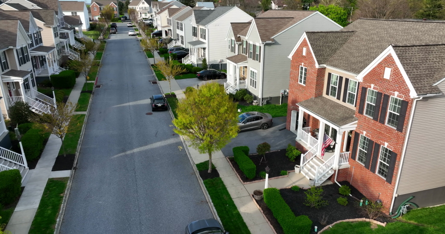 Street with two story family homes in USA. American flag at front exterior of brick house in neighborhood residential community. Aerial above street, golden hour light. | Shutterstock HD Video #1089683321