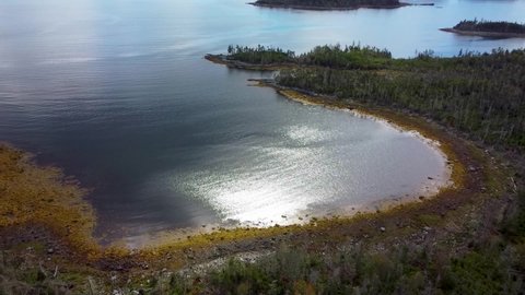 Aerial Drone Slow Motion Panorama of Sea Water Filled Cove in Atlantic Ocean Sun Reflecting off Calm Blue Water Shoreline covered in Seaweed