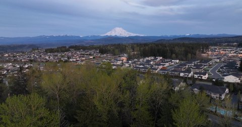 Aerial shot pushing towards Mount Rainier through trees with a large community of neighborhoods underneath.