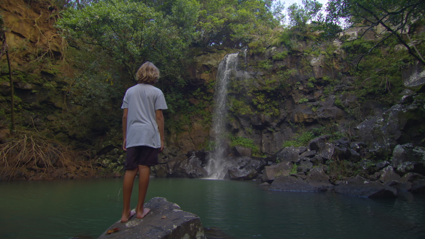 Teenager on the shore of a high, wild, beautiful waterfall. Forest rocks with a roaring stream running