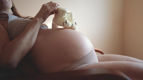pregnant woman with belly. woman with big bare a belly holding booties baby shoes close-up. health pregnancy motherhood procreation concept. indoor girl preparing for motherhood