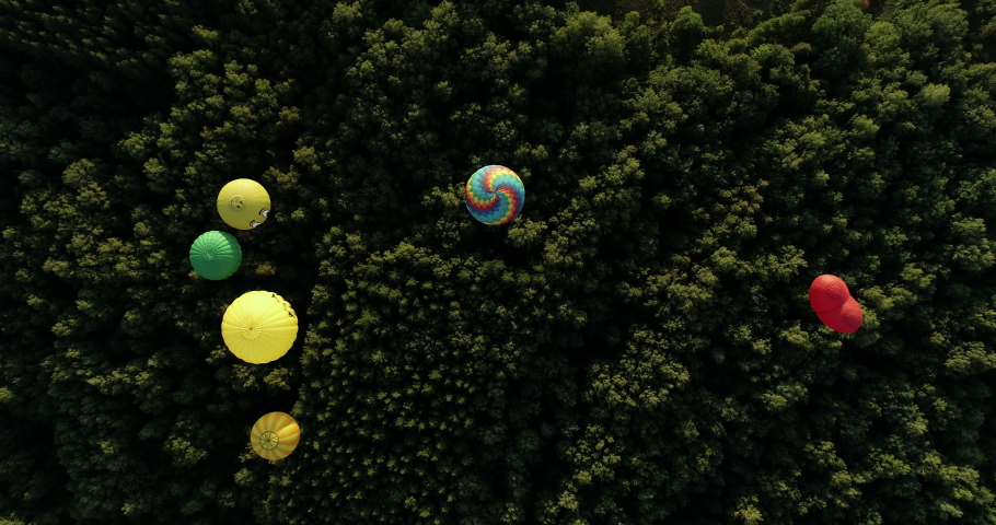 Many hot air balloons over the forest in wild lanscapes at summer sunny sunrise in the beautiful mountains background - Aerial drone view