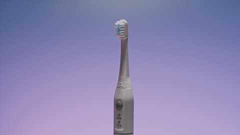 Electric ultrasonic toothbrush on shifting color background.