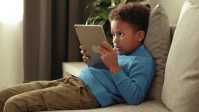 Close up cute african little boy sitting on sofa, using tablet computer. online education via internet, play games, beautiful mixed races child. 4k footage