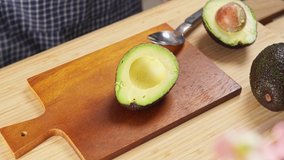 4k video, Scooping avocado flesh with a spoon. woman chef scoop avocado pulp. Cooking healthy food on wooden tray