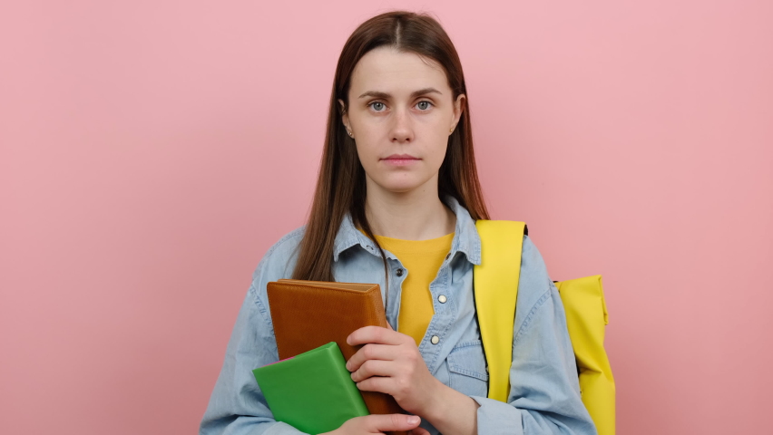 Portrait of girl teen student wears shirt and yellow backpack hold books say oops ouch oh omg, posing isolated over pink color background studio. Education in high school university college concept Royalty-Free Stock Footage #1089691845