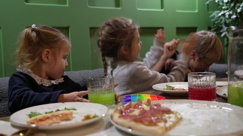 Cute boy and a girl are fighting fervently and cheerfully in a pizzeria while their sister is calmly eating pizza