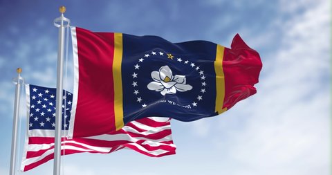 The Mississippi state flag waving along with the national flag of the United States of America. Mississippi is a state in the Southeastern region of the United States. Democracy and independence.