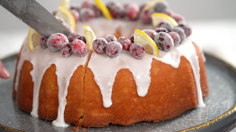 Step by step. Slicing lemon cranberry bundt cake decorated with sugar cranberries and lemon wedges.