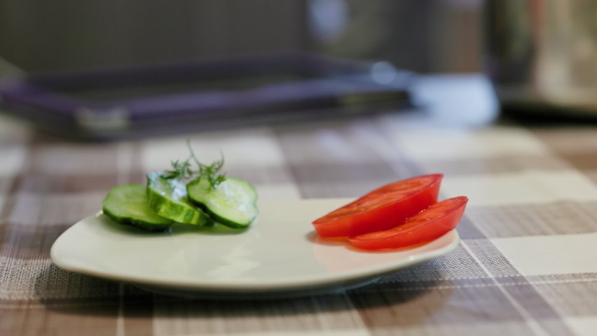 caucasian woman hand putting hot boiled potatoes with green dill and roasted chicken meat on white plate near cut tomatoes and cucumber, close-up with selective focus and slow motion