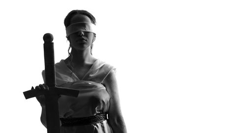 Greek goddess of justice holds sword and raises the scales. White woman blindfolded on white background lifts scale holding a sword in her hand, closeup. Concept of Greek mythology