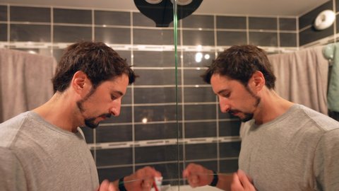 Man flossing teeth in front of bathroom mirror