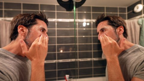 Man applying lotion cleanser washing face in front of mirror