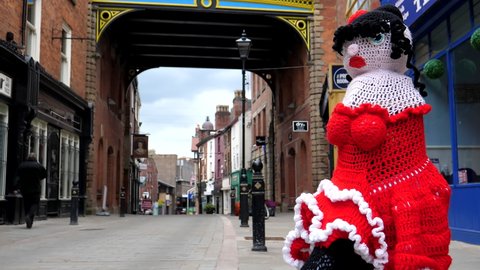 Unidentifiable senior man talking on mobile phone walking past red color rag doll mounted on street bollard in downtown of Stockport town, Greater Manchester.