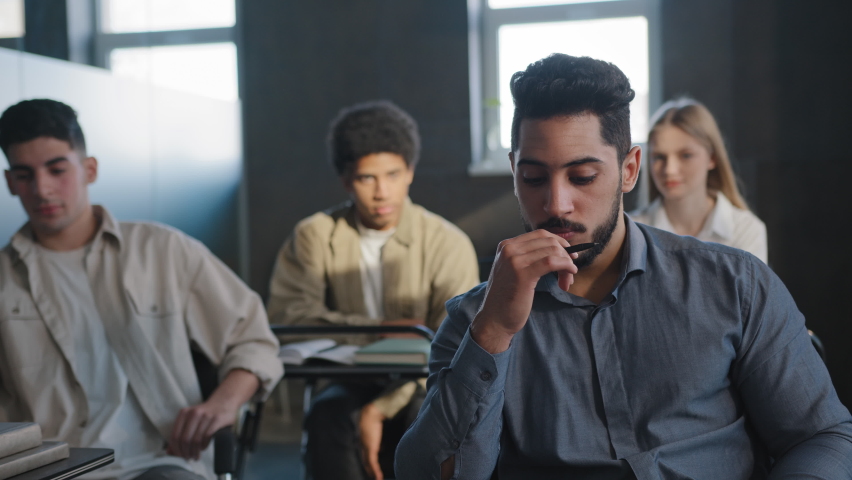 Young excited arab guy student sitting in classroom cannot concentrate on lesson being ridiculed by classmates suffering from abuse feeling distressed lonely upset concept of discrimination and racism | Shutterstock HD Video #1089696919
