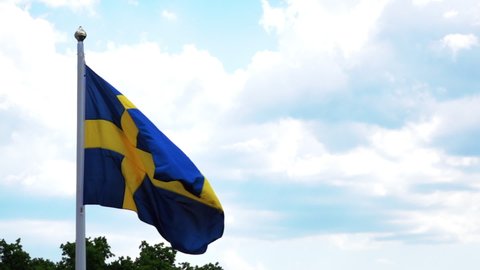 Slow Motion Lockdown Shot Of Swedish Flag Waving Against Cloudy Sky On Sunny Day - Stockholm, Sweden