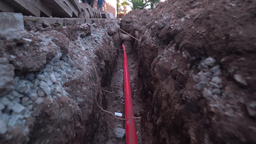 Safe connection of new isolated Internet to house, gas card, construction of system made of red metal-plastic tape lies in pit dug on city street. Top view, camera movement on stabilizer in ground. | Shutterstock HD Video #1089699637