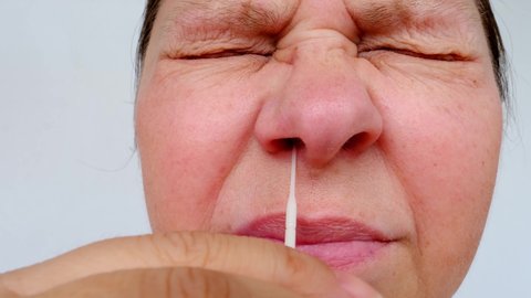 close-up of part of mature woman 50 years face, cotton swab for PCR test into female hand, person makes herself rapid test for coronavirus, concept of vaccination against coronavirus covid 19