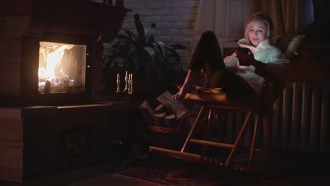 A girl sitting in a rocking chair and chatting on a self phone near the fireplace. Smiling and messaging. High quality 4k footage