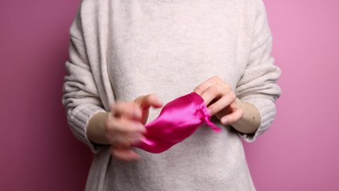 An unrecognizable woman in a sweater takes out a menstrual cup from a bag and shows it.
