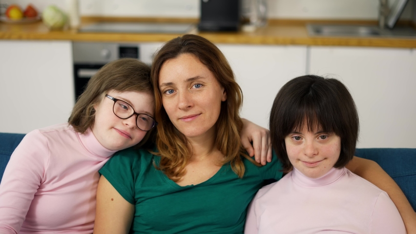 Portrait of two girls with down syndrome in sitting on a couch together embracing with their mom, close up