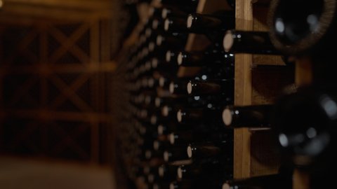 Live camera moves along rows of corked wine bottles stacked in wine cellar indoors. Expensive high-quality beverage in bodega in darkness. Luxury and winemaking concept