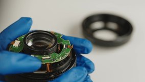 Broken camera lens in hands of master. Close up. Unrecognizable person in gloves considering breakdown before repair. Concept of repair of photographic equipment and accessories.