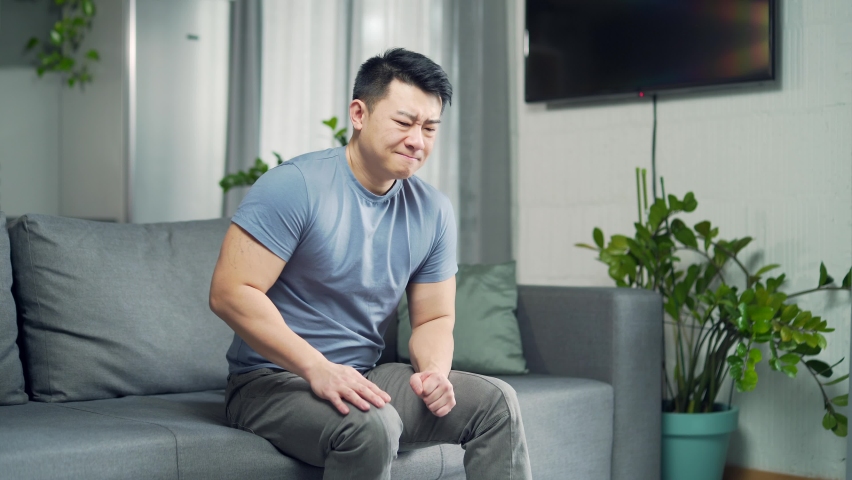 Young asian man suffering chest pain, having heart attack at home, health problem. Male Trouble breathing stroke massage sitting on couch indoors. health problems concept Royalty-Free Stock Footage #1089712351
