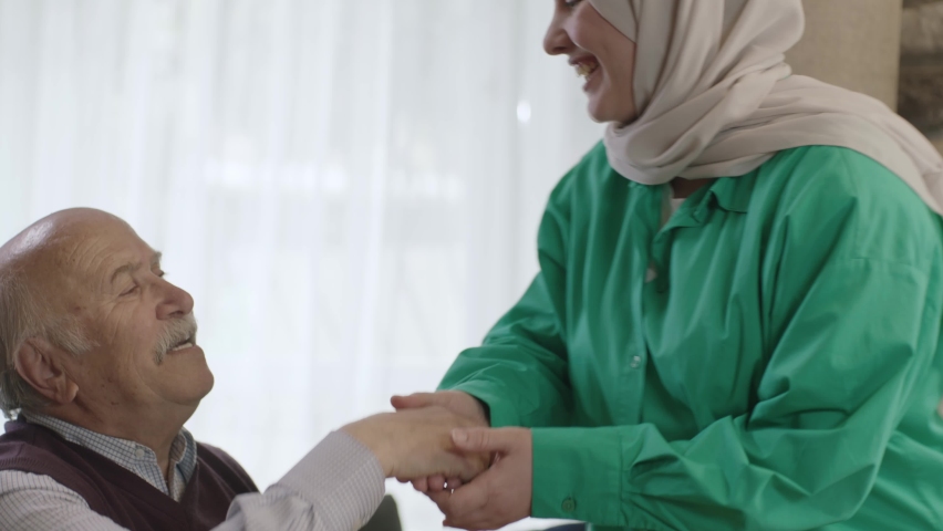 Smiling happy young woman in hijab visiting her elderly father. Adult daughter in hijab kissing her father, celebrating Eid or Father's Day. They are smiling and looking at the camera. | Shutterstock HD Video #1089714621