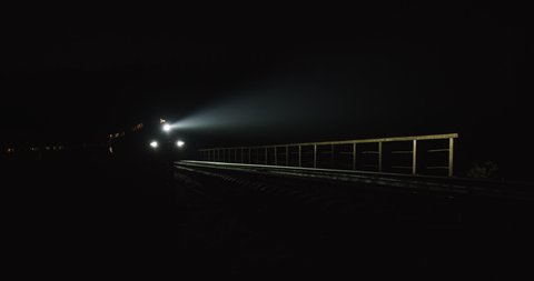 Train goes over the bridge with an old stone viaduct. The railway line at night, the train of motion, electric line. Train lights prairie railroad tracks on dark purple night