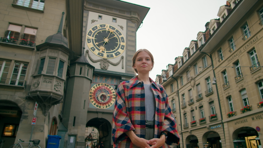 Portrait of Woman with Bern Landmark Clock Tower Zytglogge, Switzerland. Young Lady with arms crossed Looks to camera near Swiss Historic Monument in European Capital. 4K low angle hero shot