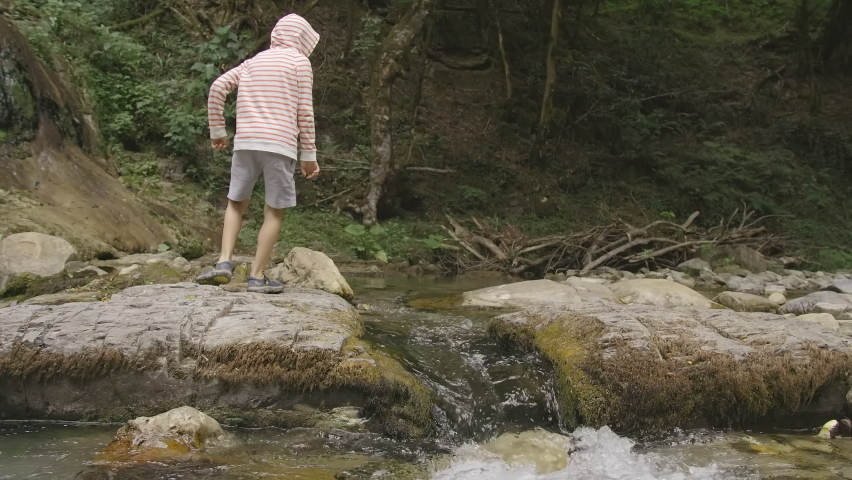 Side view of a boy jumping over the mountainous water stream. Creative. Forest lake and a boy having fun.