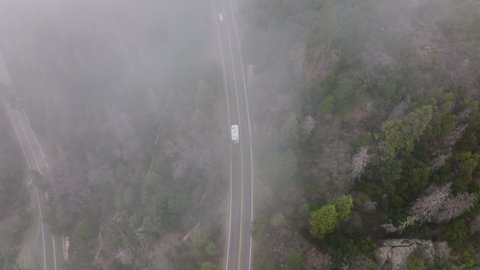Aerial top down view above mountain serpentine road with white RV vehicle bus driving up the mountain to the Sequoia National park entrance. Tourists traveling by mountains, view above clouds, USA 4K