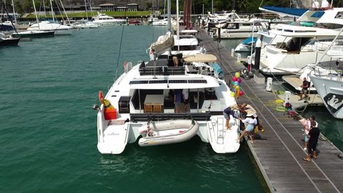Phuket, Thailand, 24, February,2022:
Tourists board a sailing catamaran in a yacht marina, drone view of passengers preparing to embark on a sea voyage